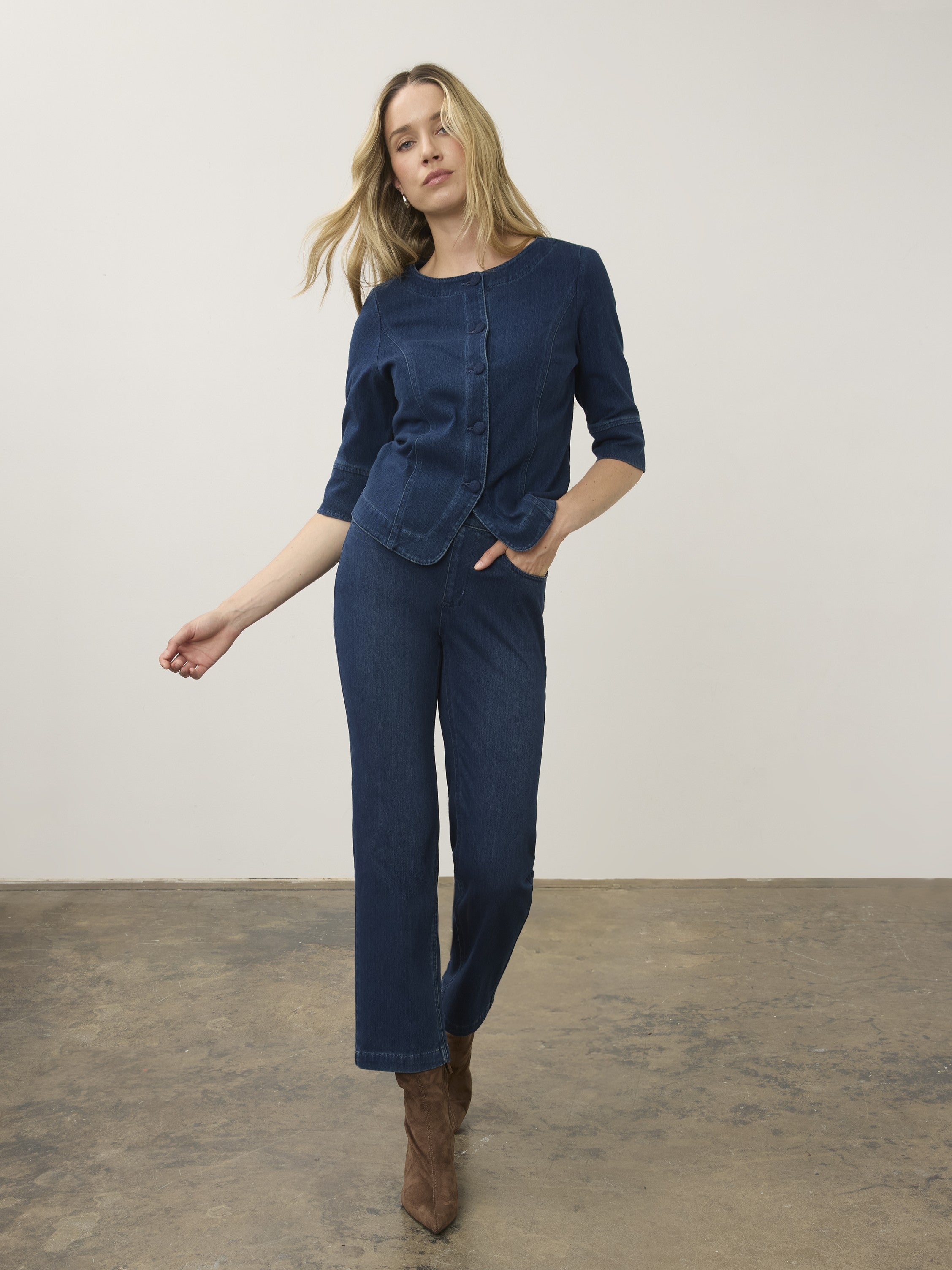 Individual wearing a dark blue denim jacket with three-quarter sleeves and matching denim pants and brown boots.
