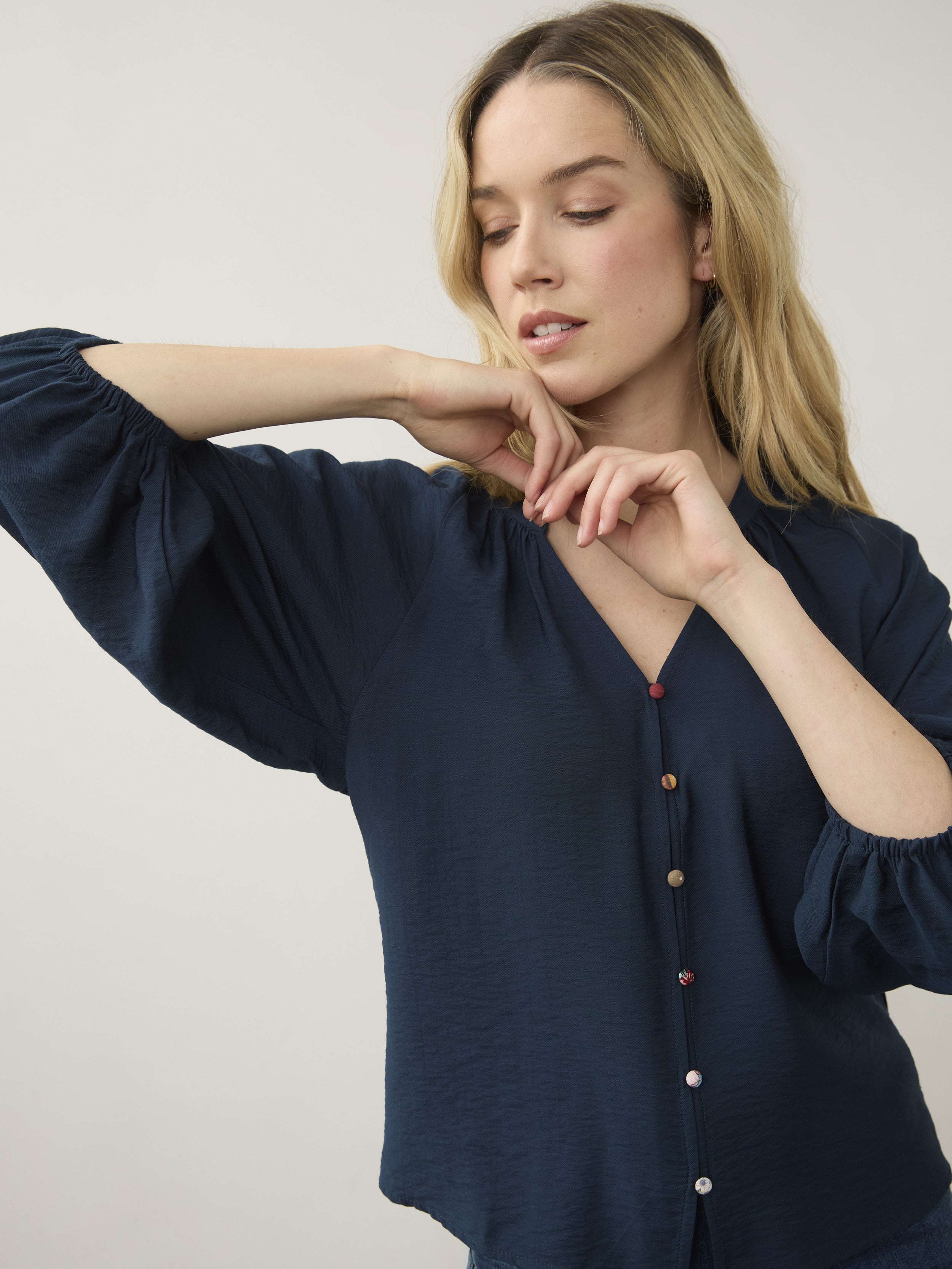 Navy blue long-sleeve blouse with gathered sleeves and multicolored buttons on a light background.