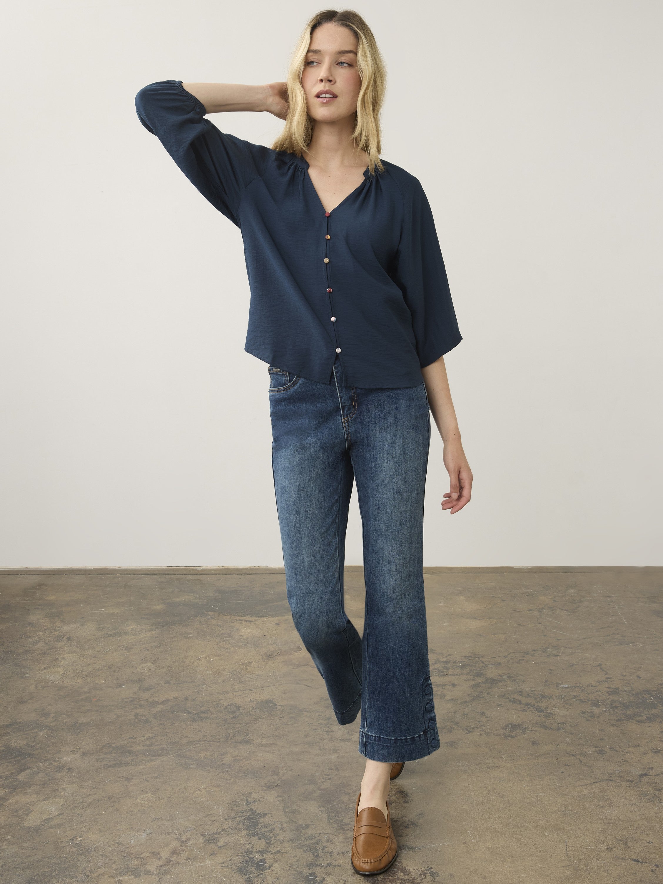Navy blue button-up top paired with wide-leg denim jeans and brown slip-on shoes on a plain background.