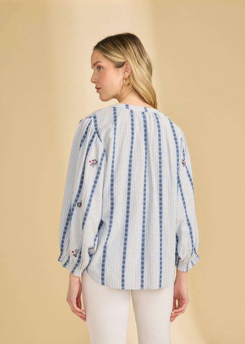 Lightweight long-sleeve blouse with blue vertical stripes and floral embroidery on sleeves against a beige background