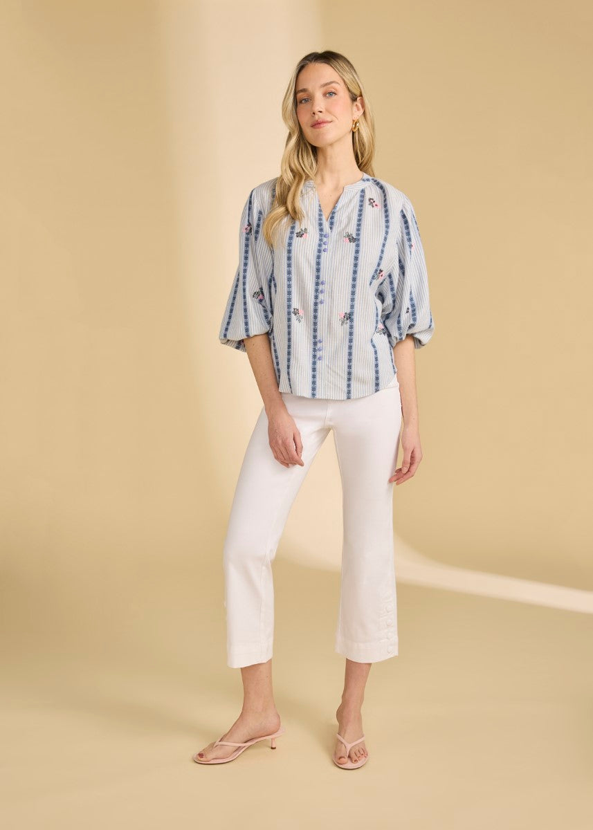 Person wearing a striped blue and white top with floral details paired with white cropped pants and sandals