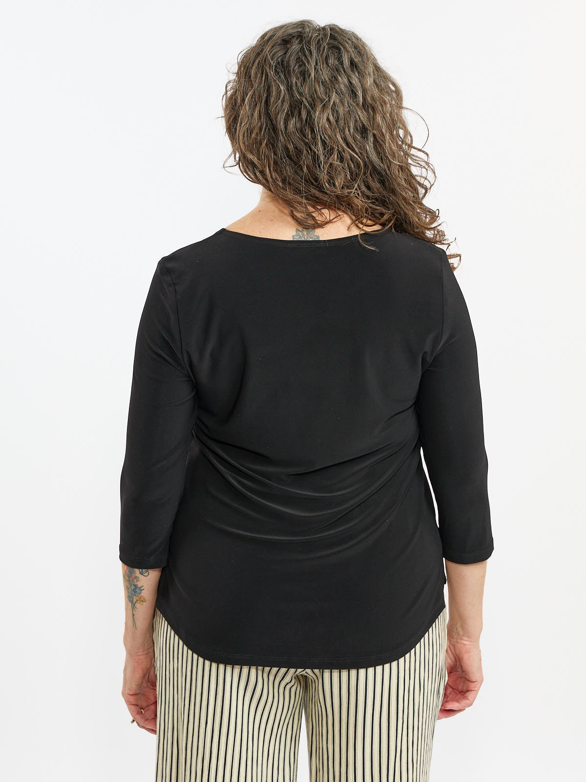 Back view of a black three-quarter sleeve top paired with light-colored striped pants against a plain background.