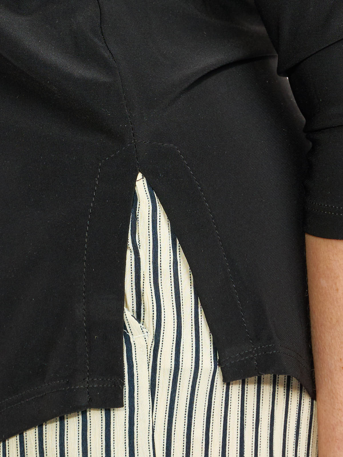 Close-up of black outerwear side slit revealing a vertically striped white and navy fabric underneath.