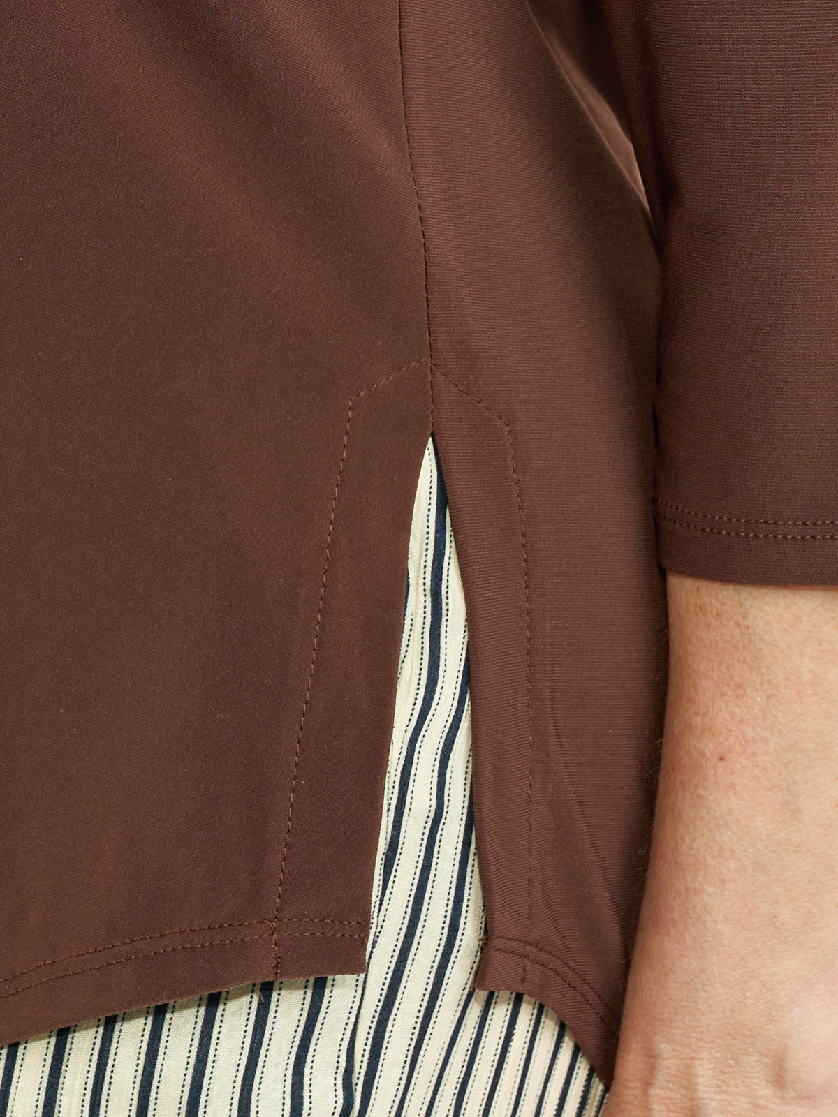 Close-up of brown fabric split hem revealing striped inner layer with visible stitching and part of a short sleeve.