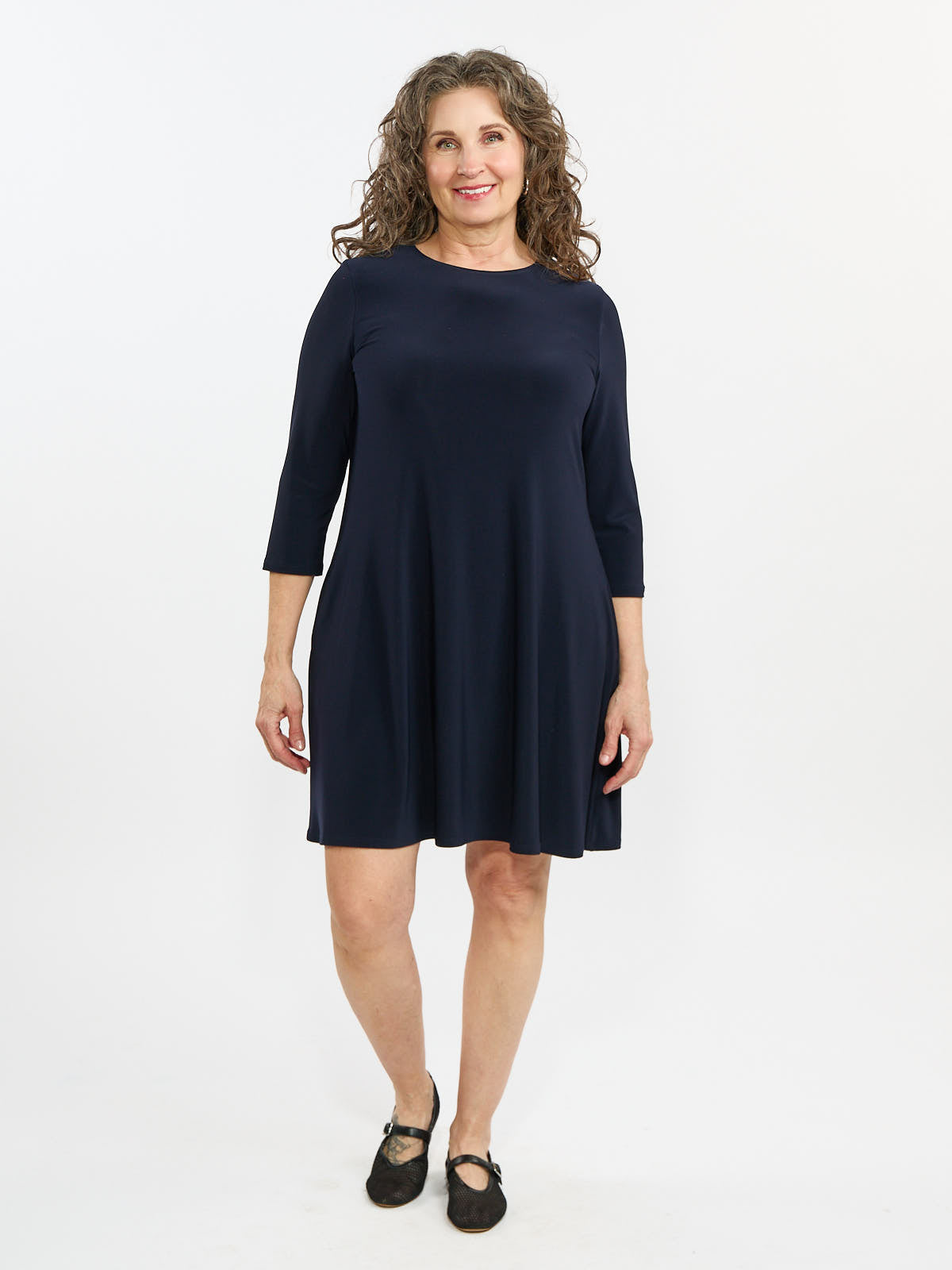 Woman in a navy blue knee-length dress with three-quarter sleeves and black Mary Jane shoes standing against a white background