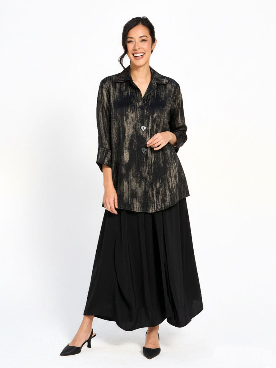 Smiling model in a black patterned blouse and flowing black skirt against a white background