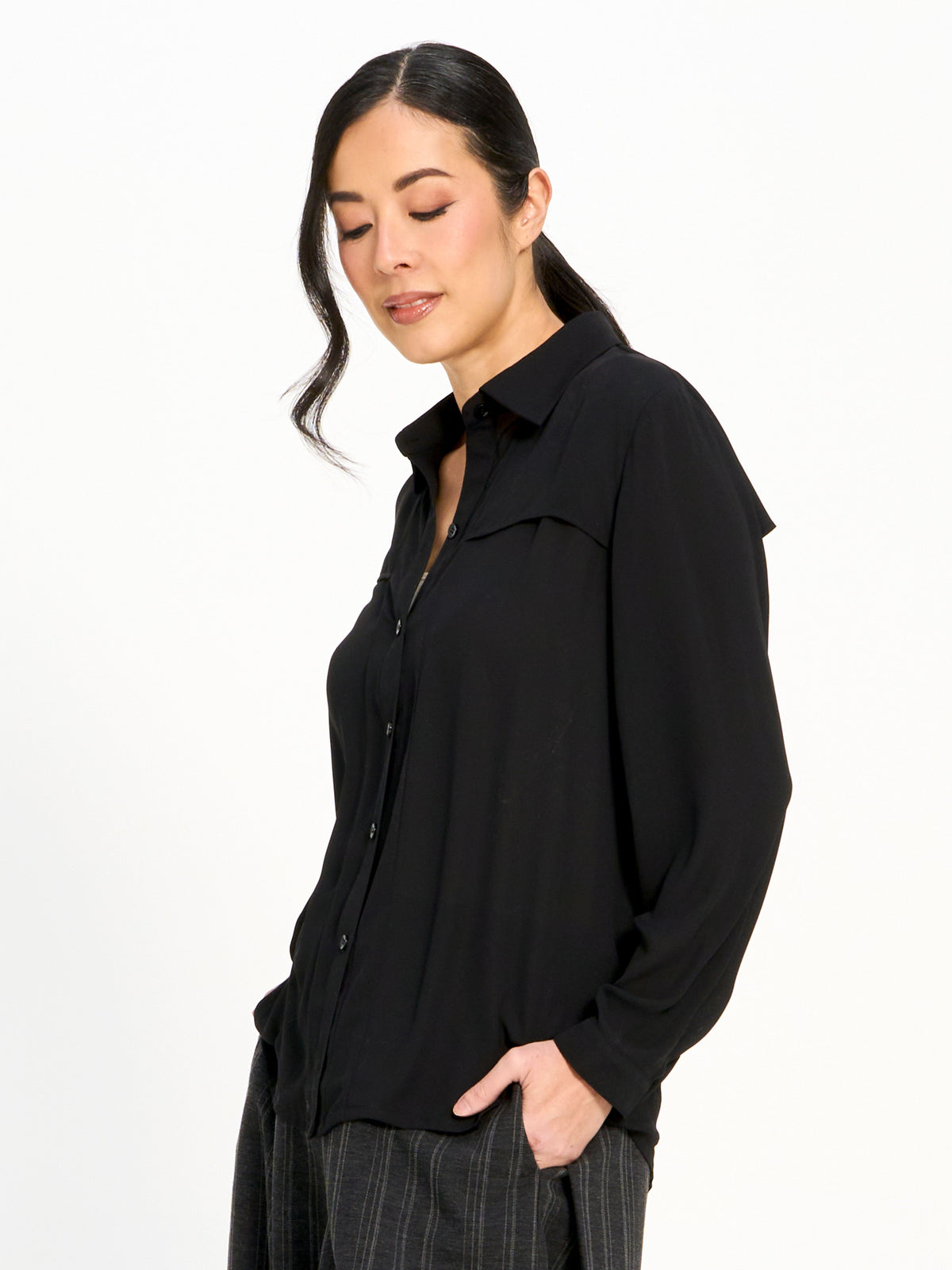 Side view of a long-sleeve black button-up shirt paired with dark pinstriped pants against a white background