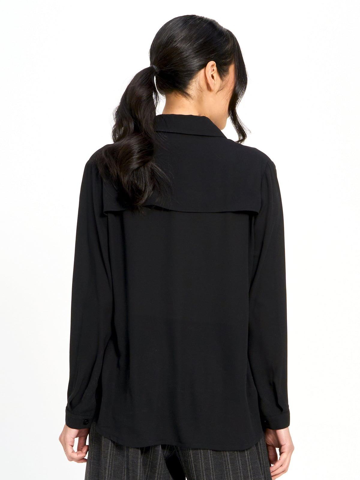 Back view of a long-sleeve black blouse with a yoke detail on the upper back and cuffed sleeves