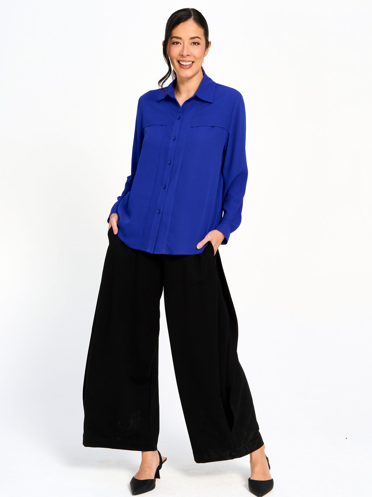 Blue button-up long sleeve shirt paired with wide-leg black pants and black pointed shoes on white background