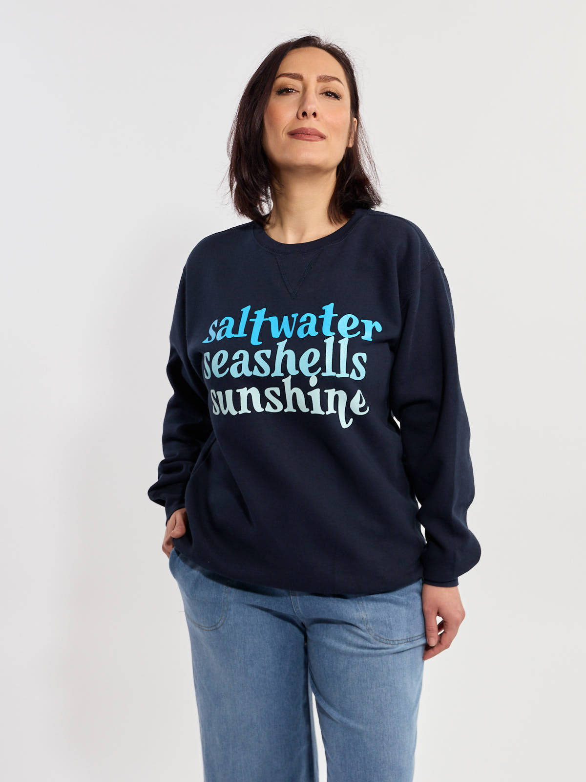 Navy sweatshirt with light blue text reading saltwater seashells sunshine paired with light blue denim jeans