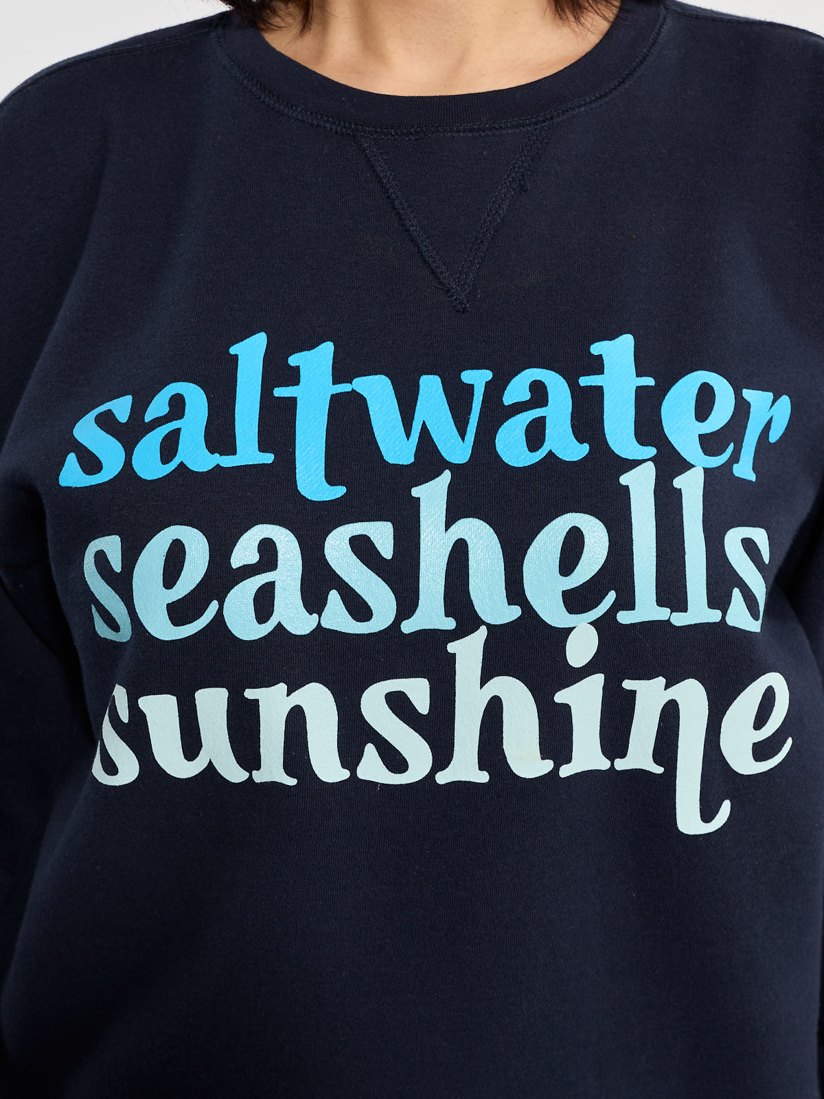 Close-up of navy blue Women’s Saltwater Seashells Sunshine Graphic Crewneck Sweatshirt by Win.E with blue text print on front