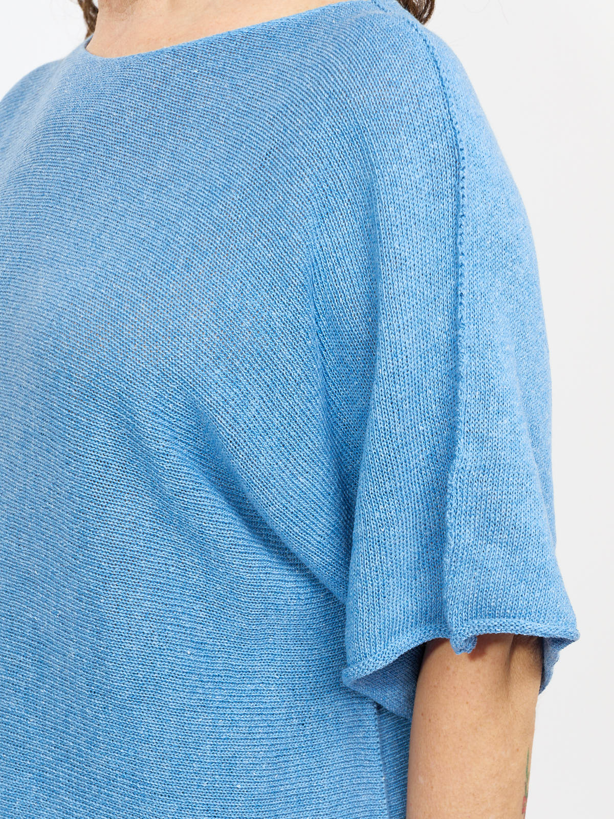 Close-up of a blue knitted short-sleeve top with a loose fit and visible seam along the shoulder.