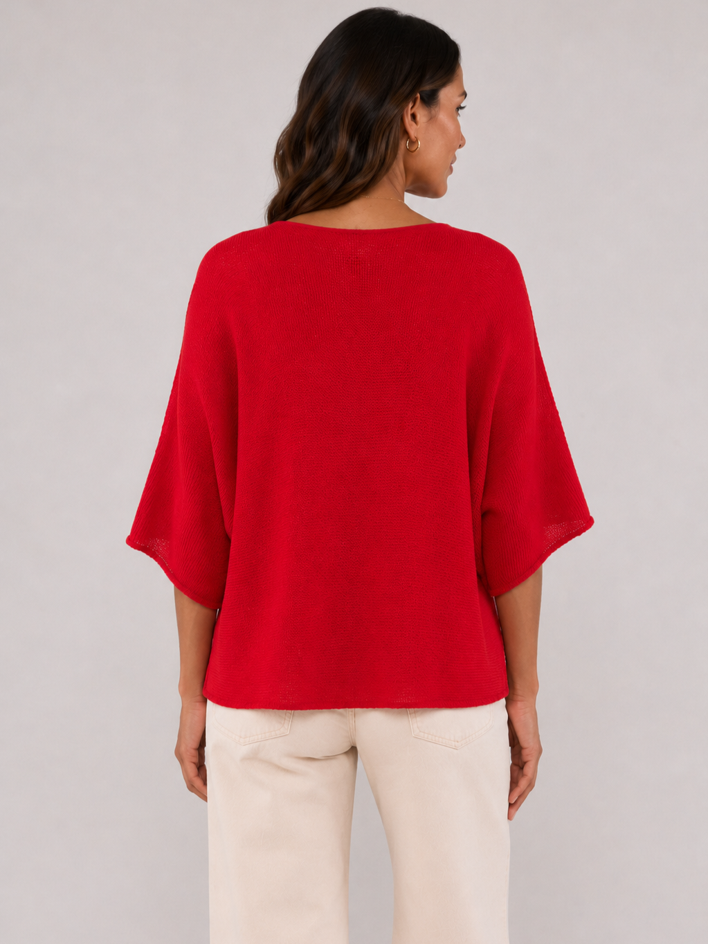 Back view of a loose red knitted top with elbow-length sleeves paired with light beige pants against a plain background.