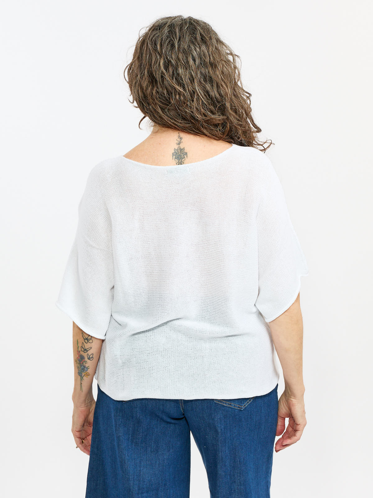 White loose-knit short sleeve top paired with dark blue denim jeans shown from the back