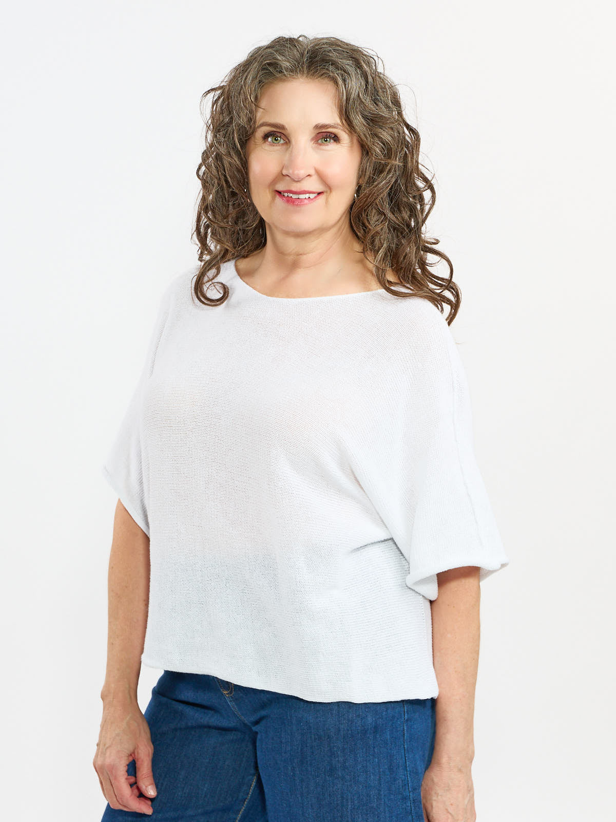 White Pop Me Over Oversized 3/4 Sleeve Knit Top by Plum Loco paired with blue denim pants, studio background.