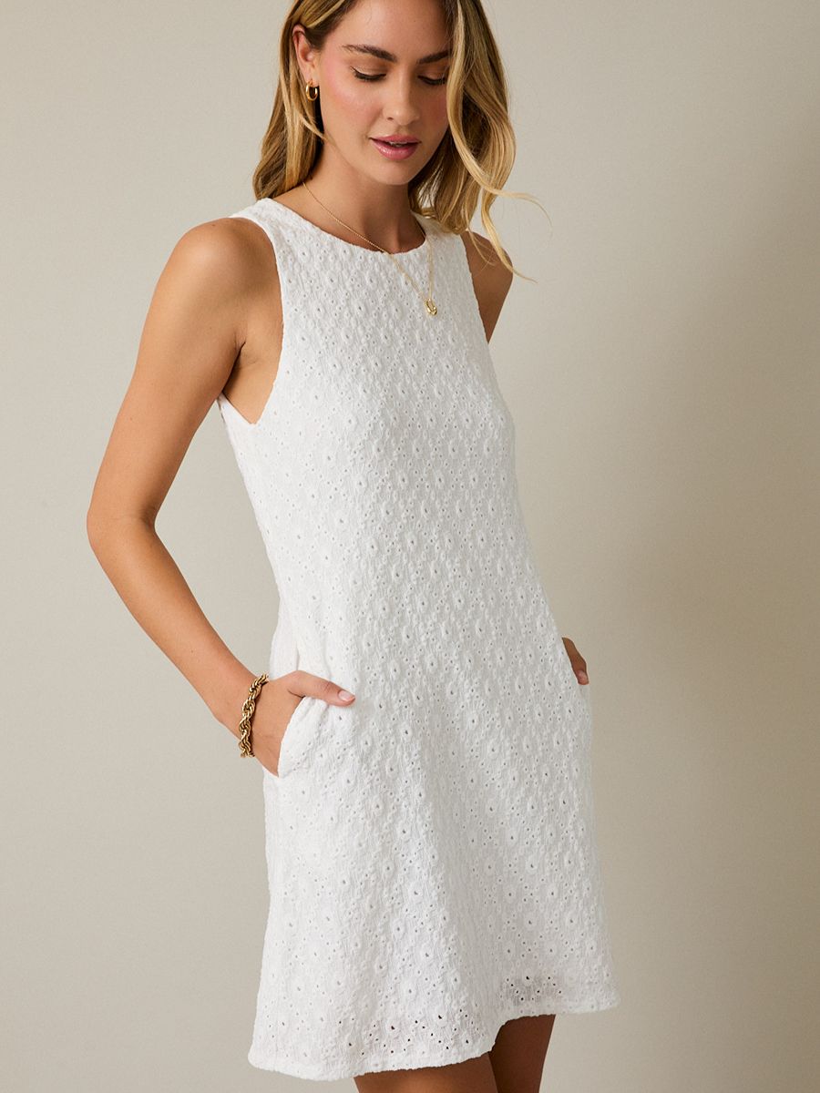 Sleeveless white eyelet dress with pockets and a subtle floral pattern on a neutral background