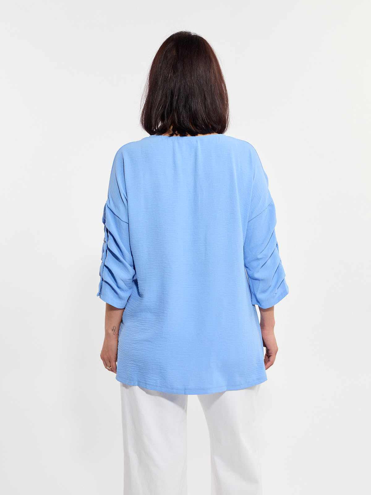 Light blue long-sleeve top with button details on sleeves paired with white pants against a plain background.