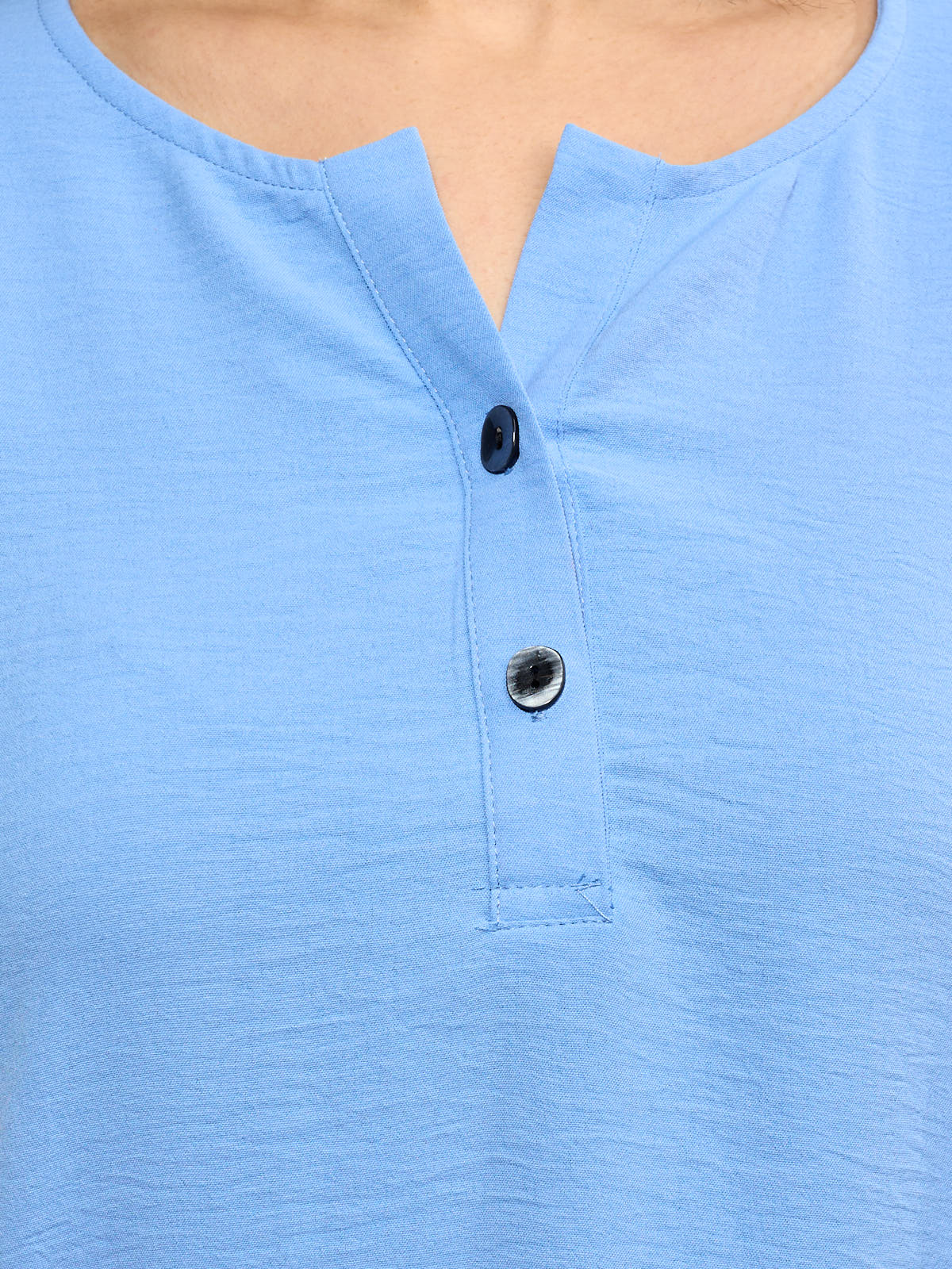 Close-up of a light blue top with a notched neckline and two decorative buttons on the front placket.