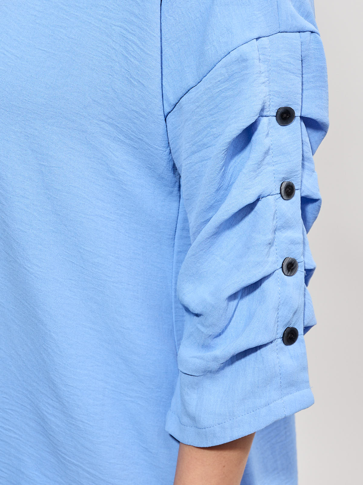 Light blue fabric sleeve with gathered detail secured by four black buttons along the outer arm seam