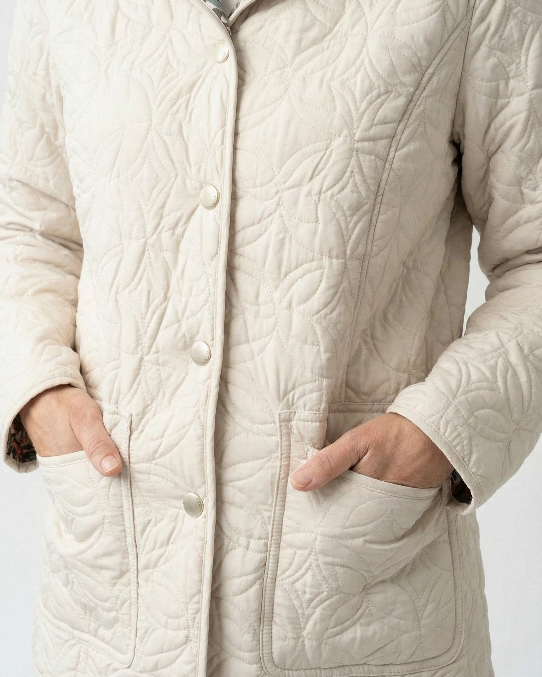 Close-up of cream quilted outerwear with floral stitching and front pockets, Lily Floral Reversible Quilted Jacket by Creations.