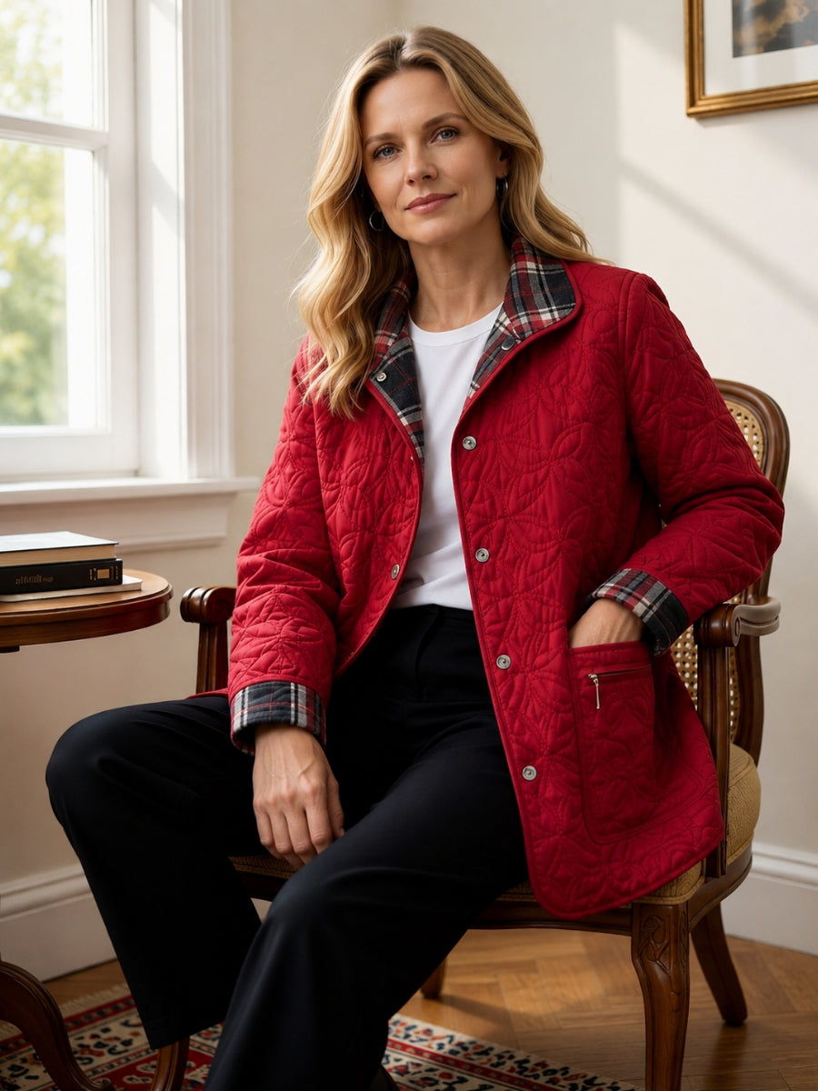 Person seated indoors wearing a red quilted jacket with plaid collar and cuffs, black pants, and a white top.