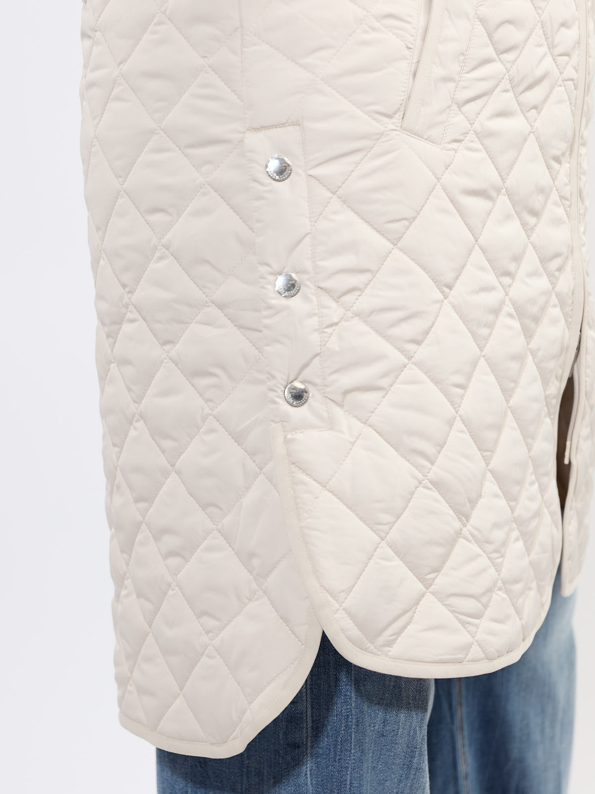 Close-up of cream quilted fabric and snap buttons on Ilse Jacobsen Quilted Vest layered over denim jeans
