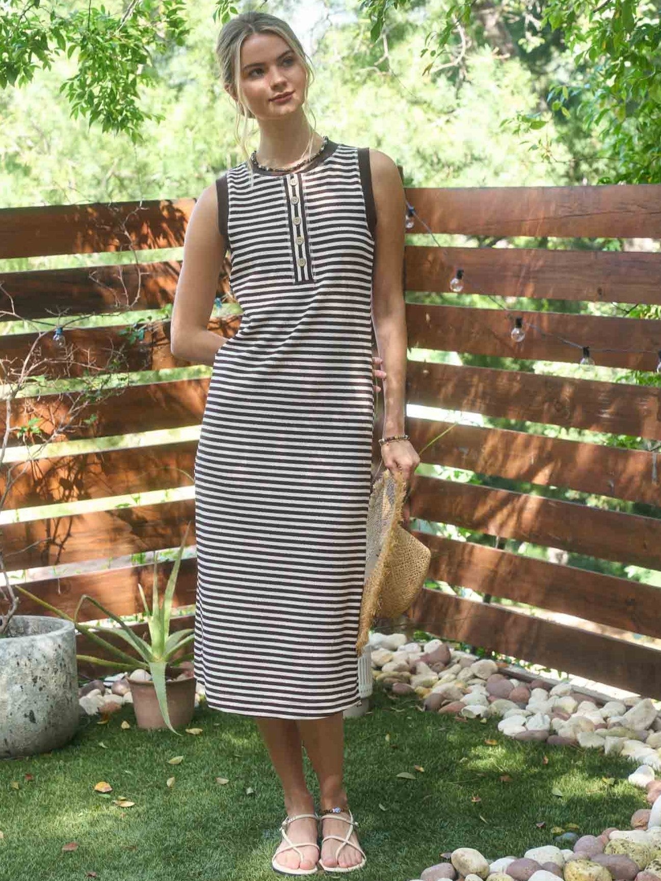 Outdoor summer scene with a model in a brown and cream Striped Button-Front Sleeveless Dress by Mine