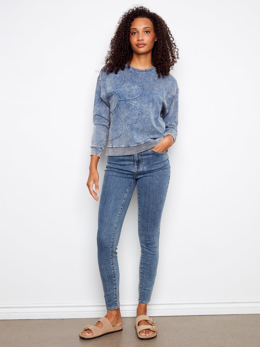 Charlie B Daisy Washed Terry Crew Neck Sweatshirt in denim blue with floral applique, styled with jeans and sandals
