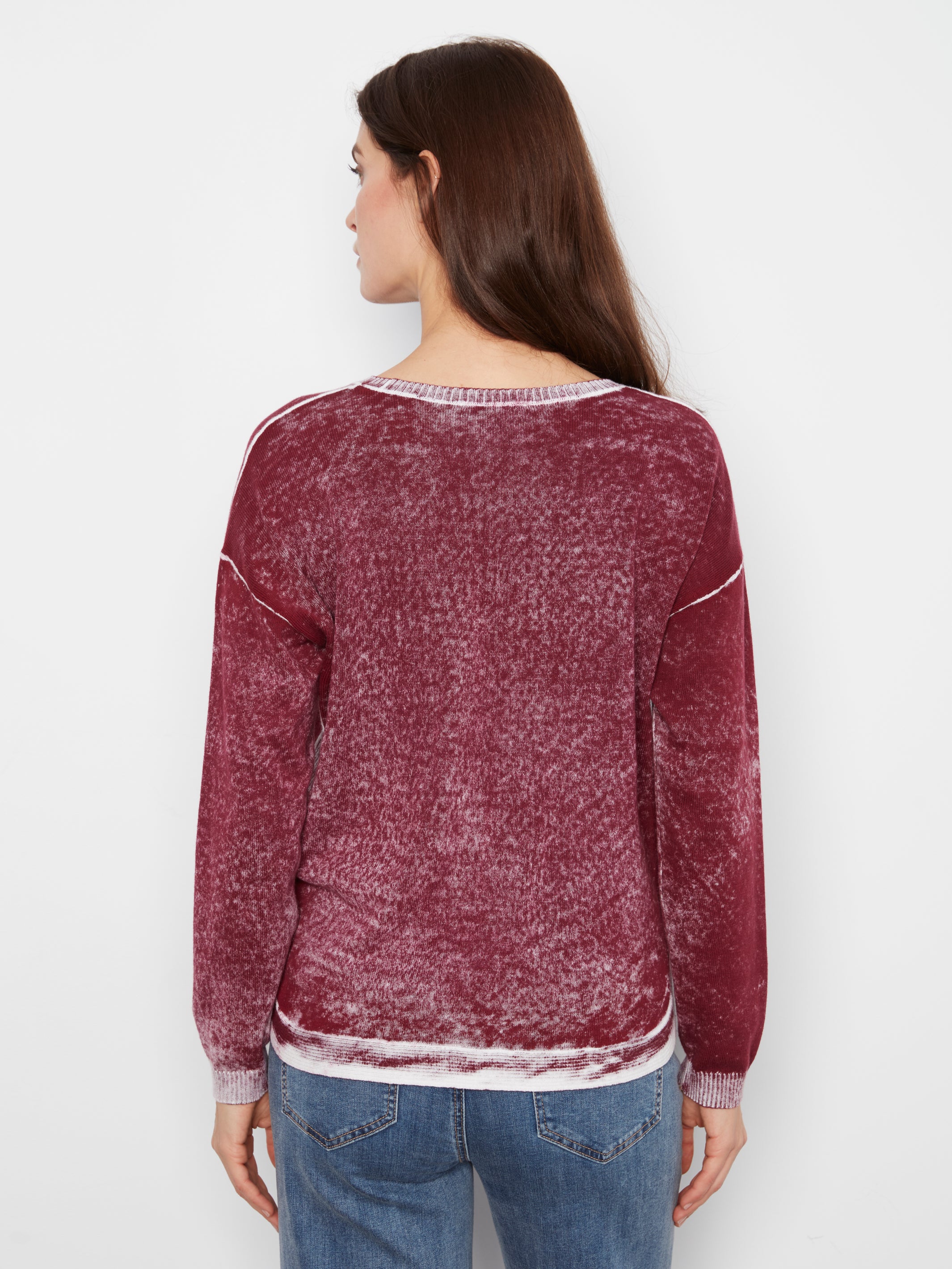 Back view of a long-sleeve, textured burgundy sweater paired with blue denim jeans on a plain background.