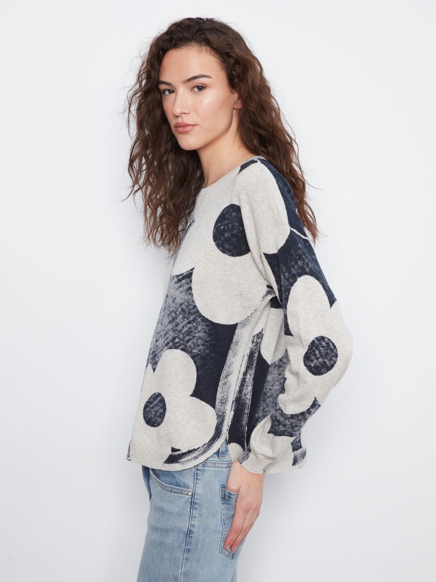 Side view of a person wearing a long-sleeve sweater with large navy and cream floral patterns and light blue jeans.
