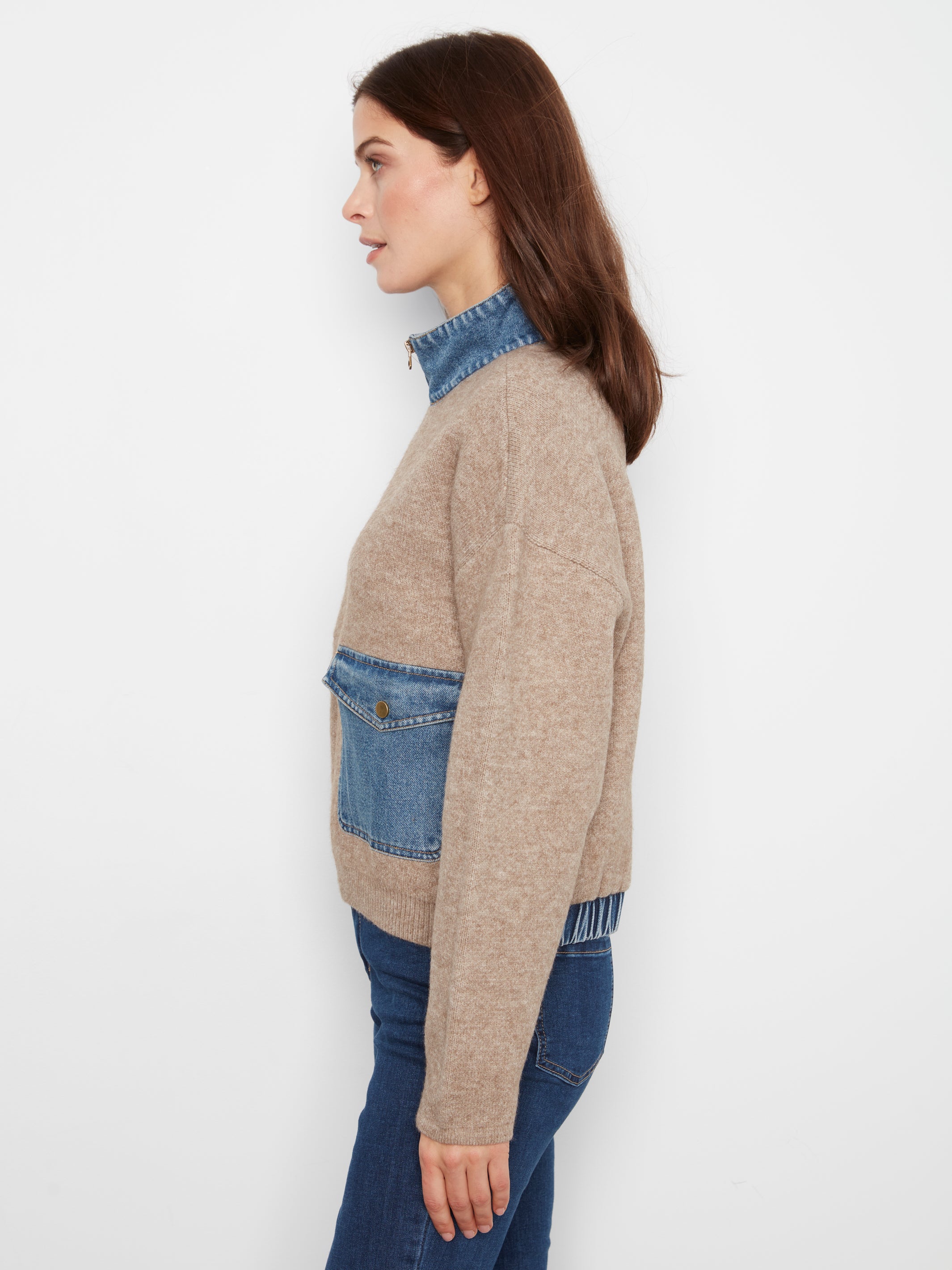 Side view of a beige sweater with denim collar and large front pocket paired with blue denim jeans.