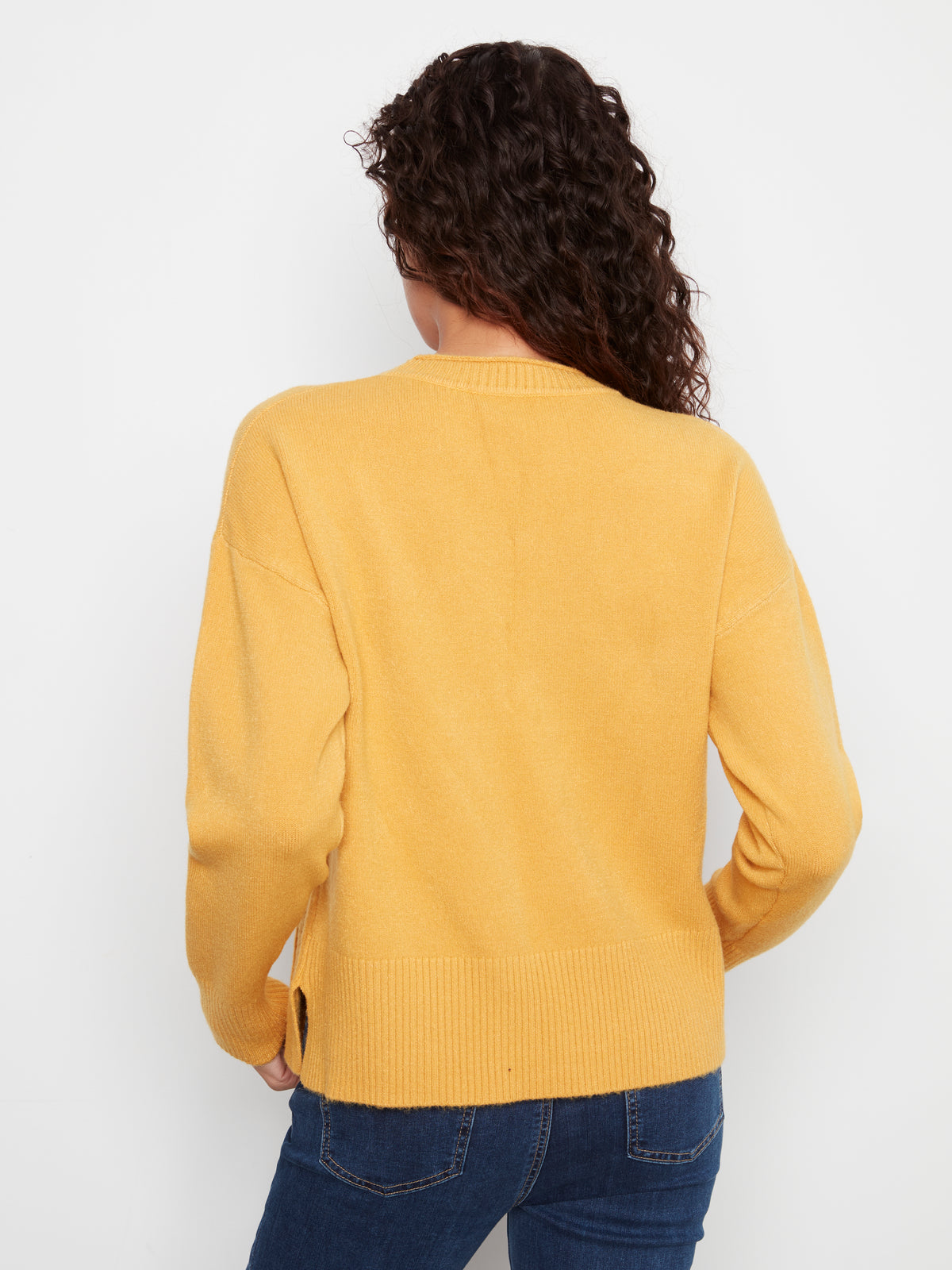 Back view of a mustard yellow knit sweater paired with blue denim jeans against a white background.