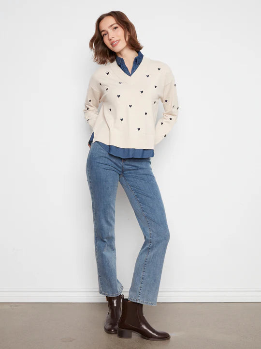 Light beige sweater with small heart patterns over dark blue shirt paired with blue denim jeans and dark ankle boots.