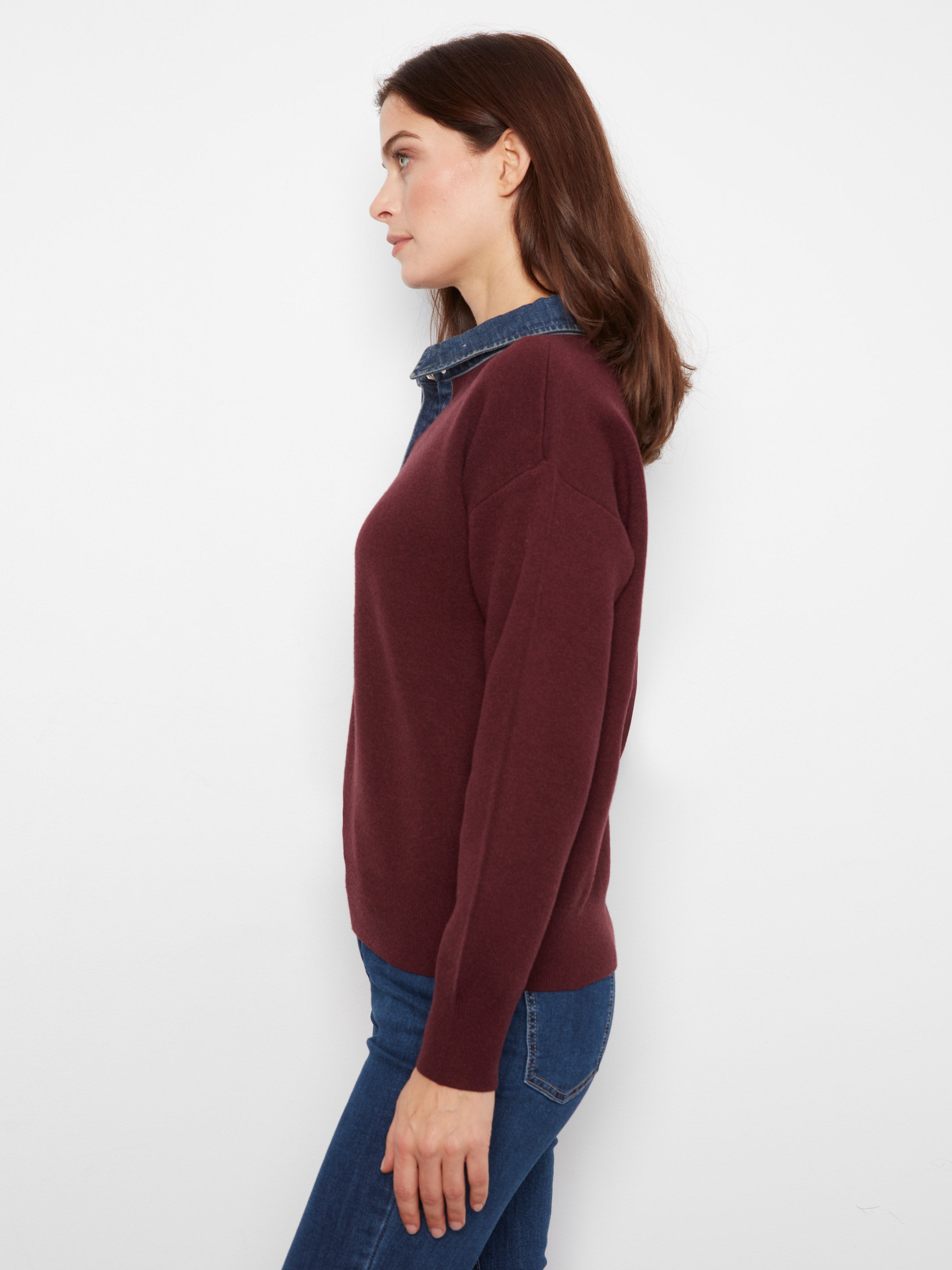 Side view of a burgundy sweater over a denim shirt paired with blue jeans against a plain white background.