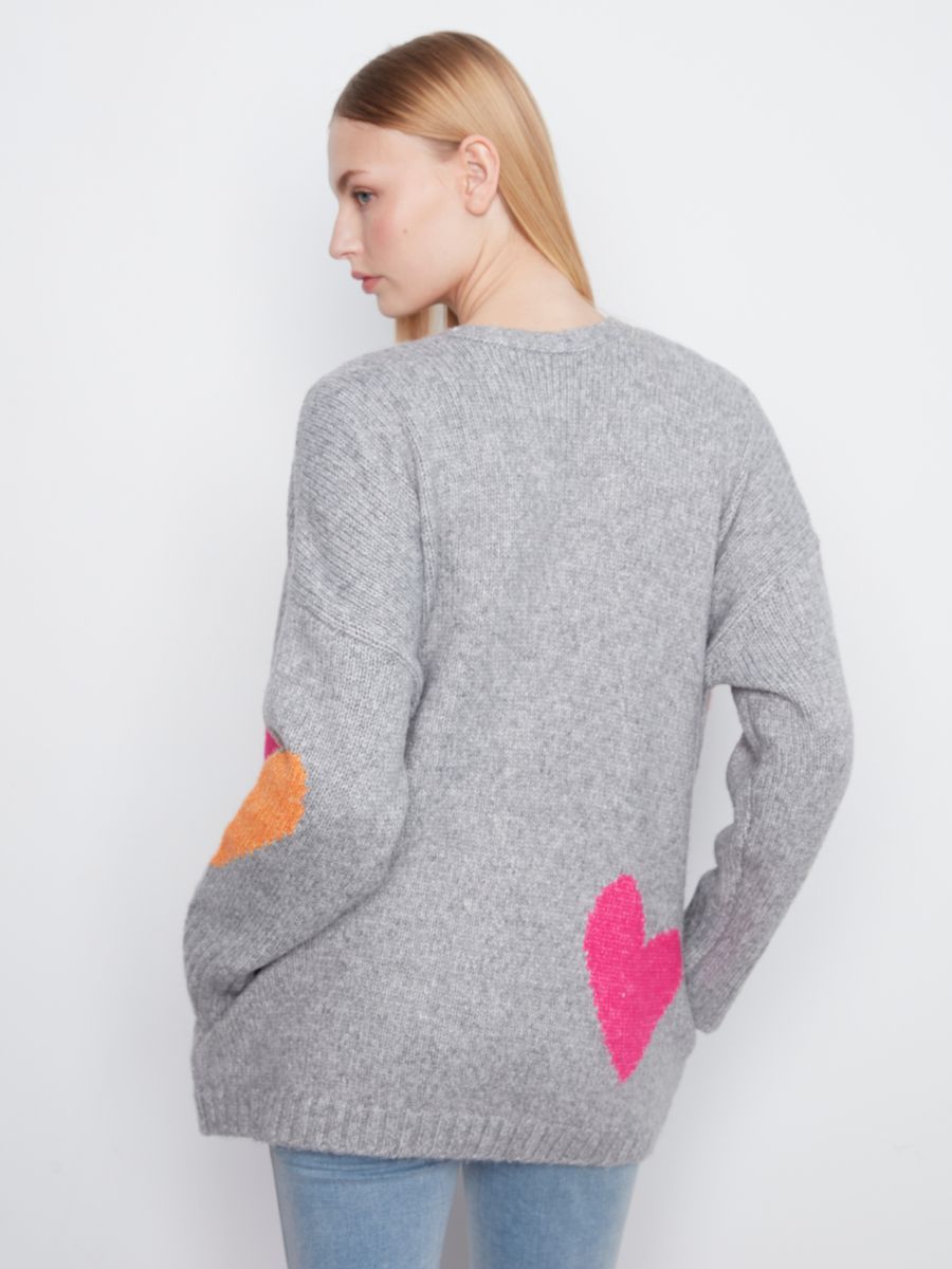 Light grey knitted sweater with bright pink and orange heart shapes on the back and sleeve, worn with blue jeans.