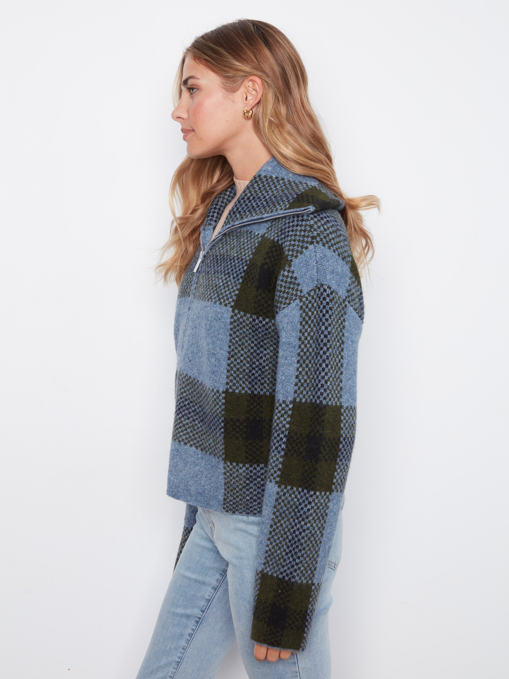 Profile view of a zip-up blue and green plaid wool sweater worn with light blue denim jeans.