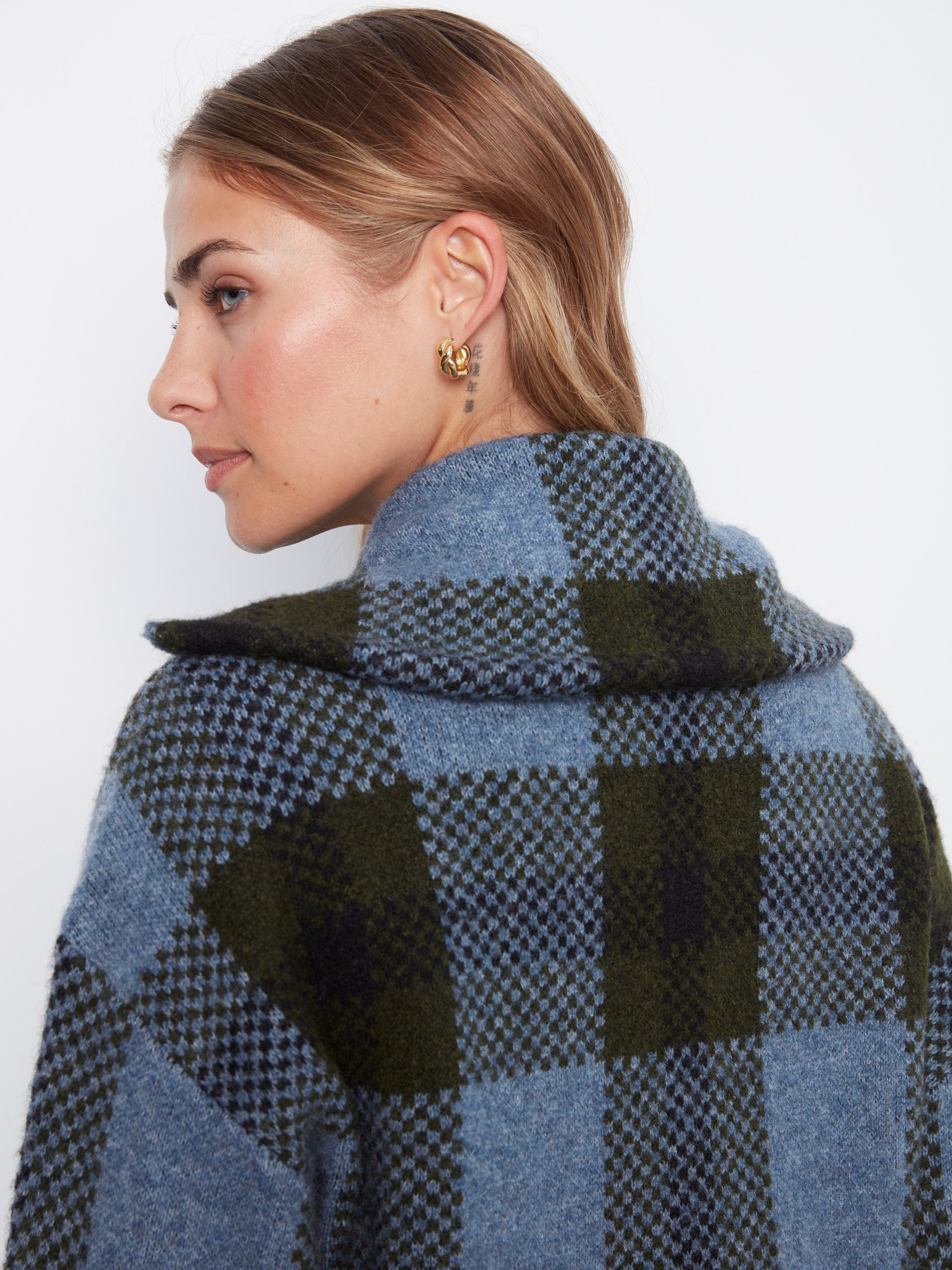 Close-up of a blue and green plaid wool coat with a high collar and gold hoop earrings visible.