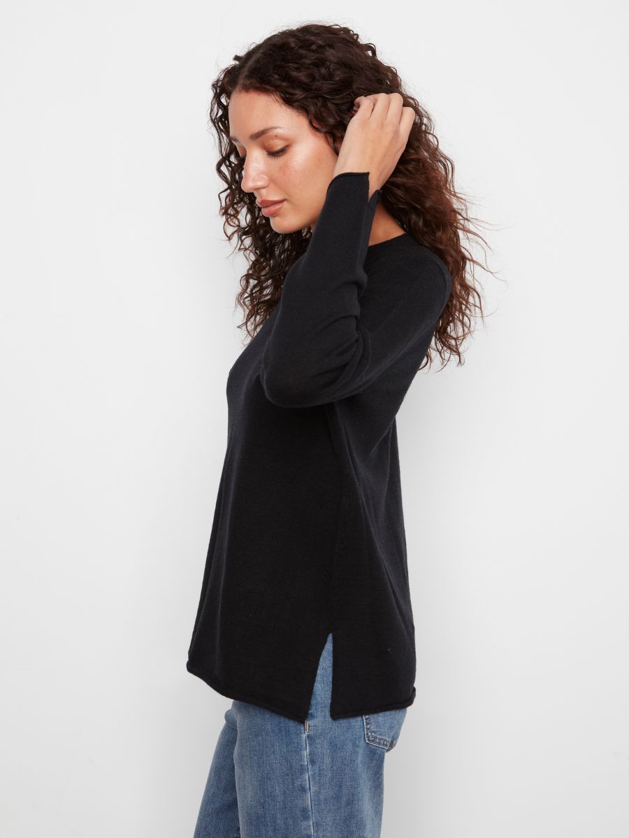 Side view of a black long-sleeve sweater with side slits paired with blue denim jeans on a neutral background.