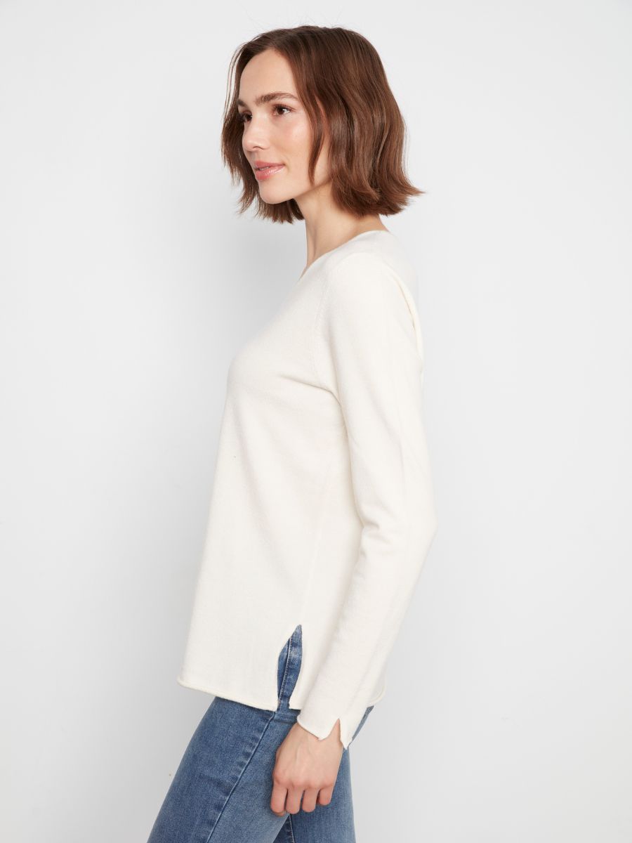 Side view of a person wearing an off-white long-sleeve sweater paired with blue denim jeans against a plain background.