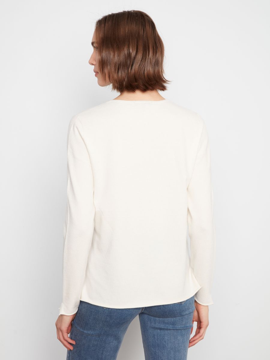 Back view of a long-sleeve ecru sweater paired with mid-blue denim jeans against a plain background.