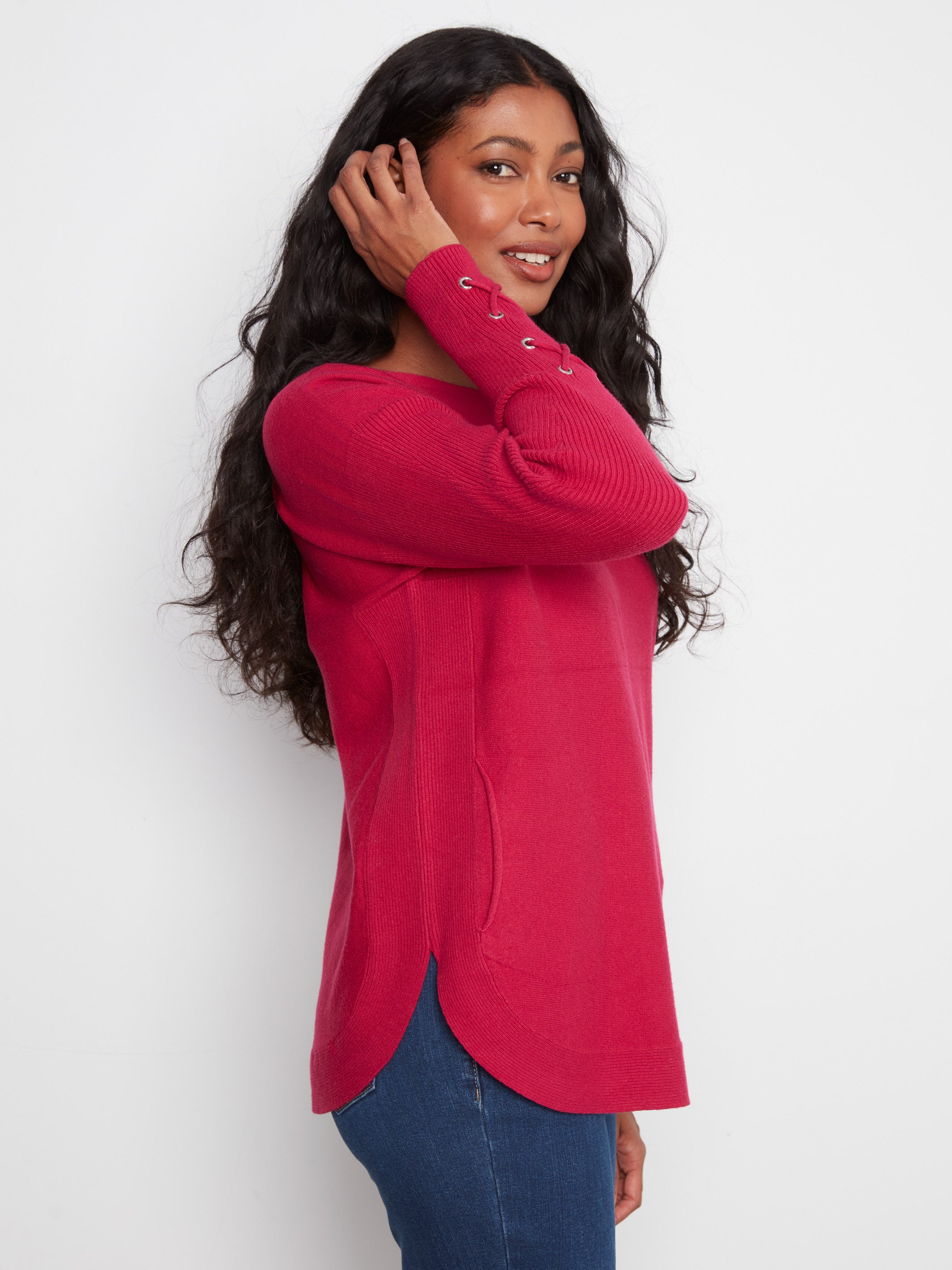 Side view of a red sweater with lace-up cuff details paired with blue denim jeans against a plain background.