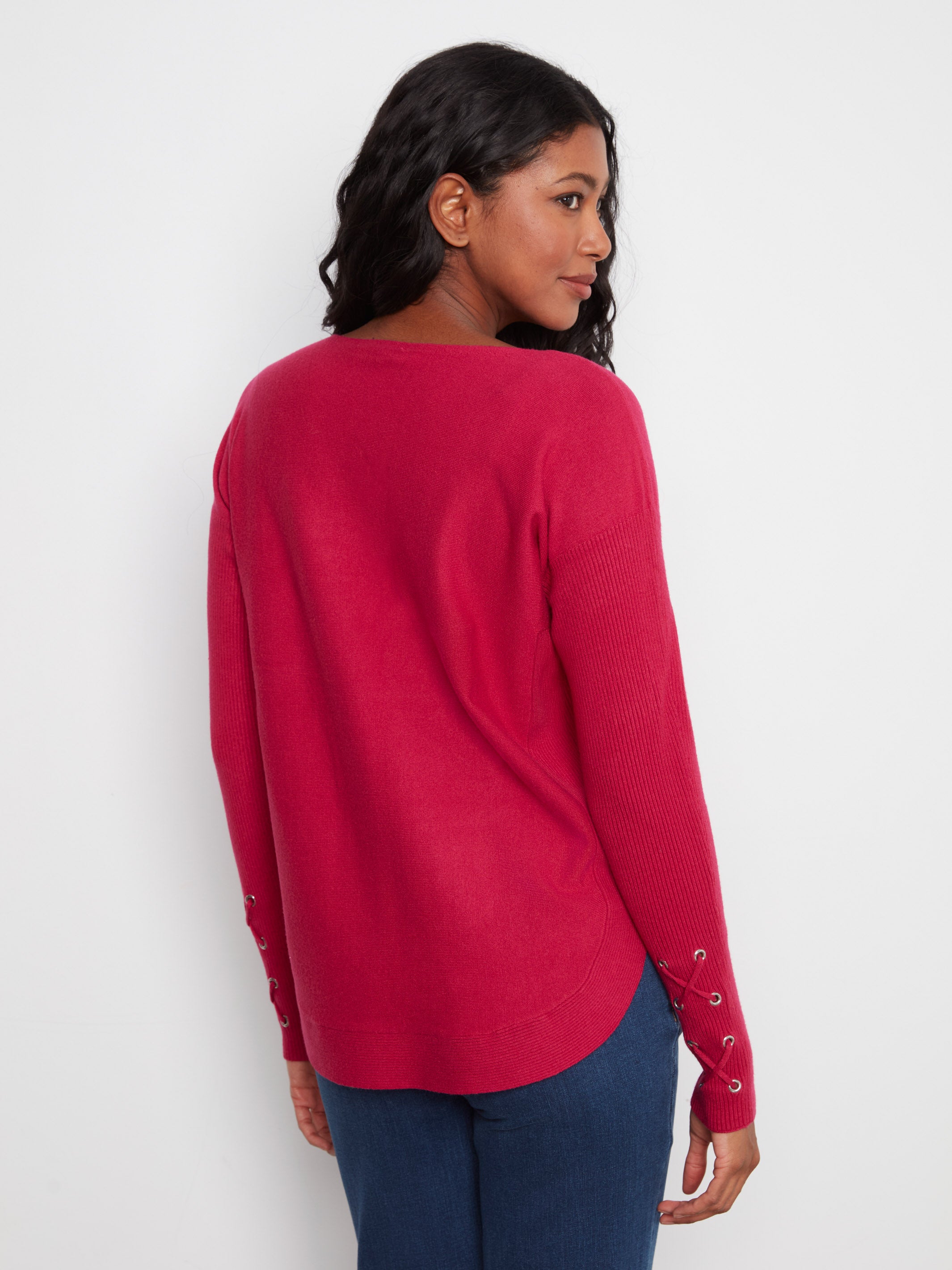 Rear view of a red sweater with lace-up details on the sleeves paired with dark blue denim jeans.