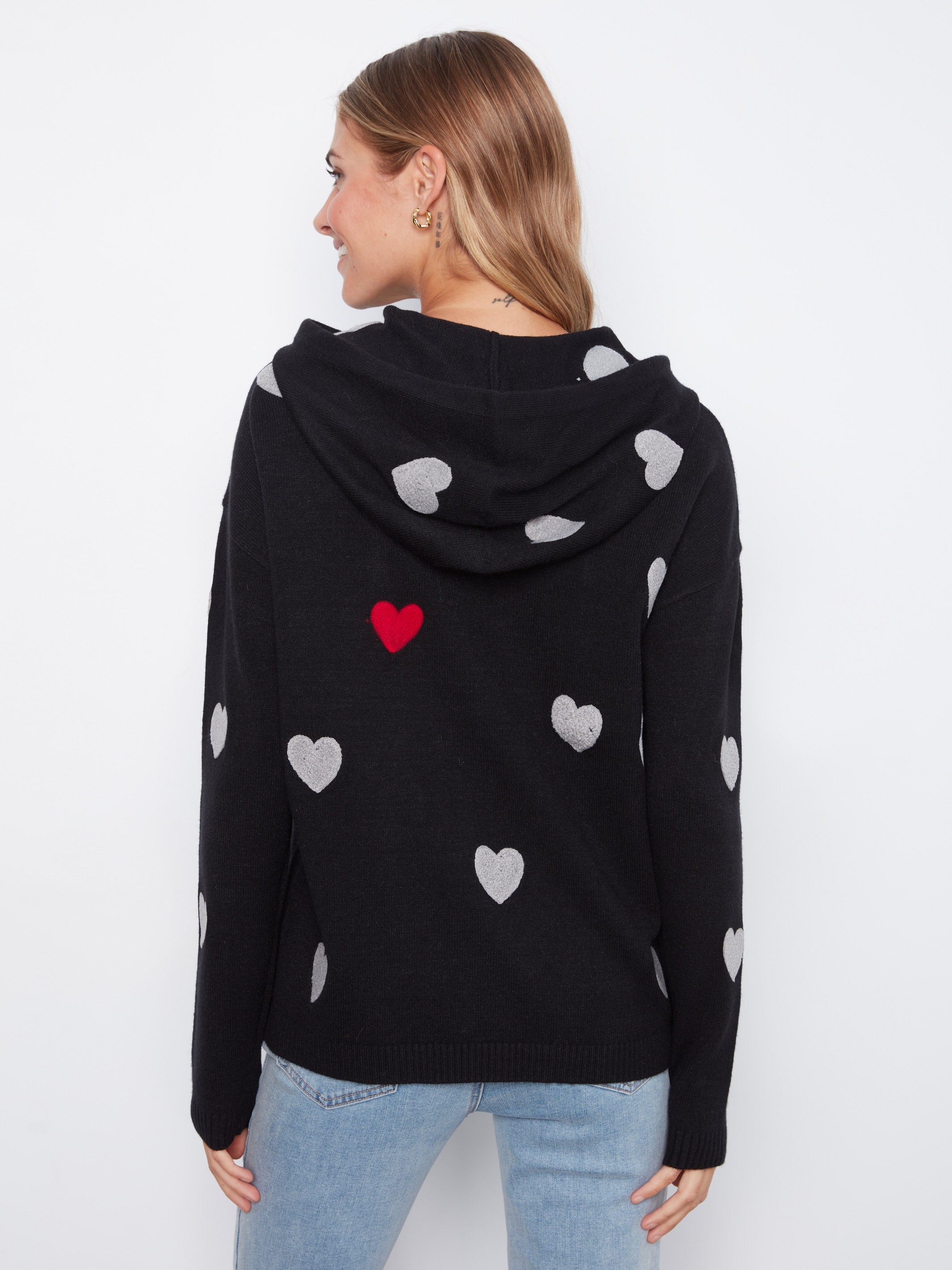Black hooded sweater with white and one red heart patterns paired with light blue denim jeans viewed from the back