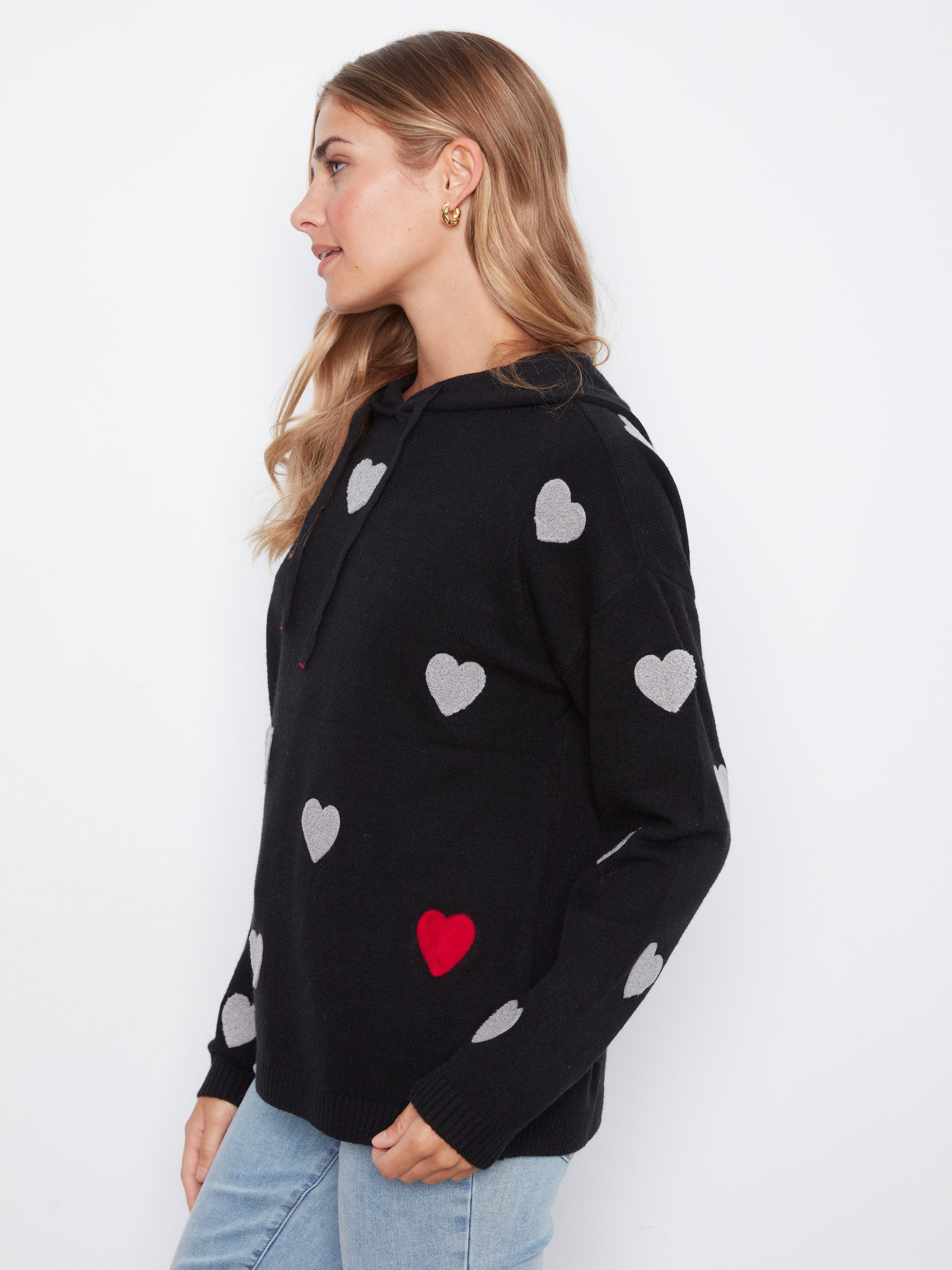 Side view of a black hoodie sweater with gray and one red heart pattern paired with light blue jeans.