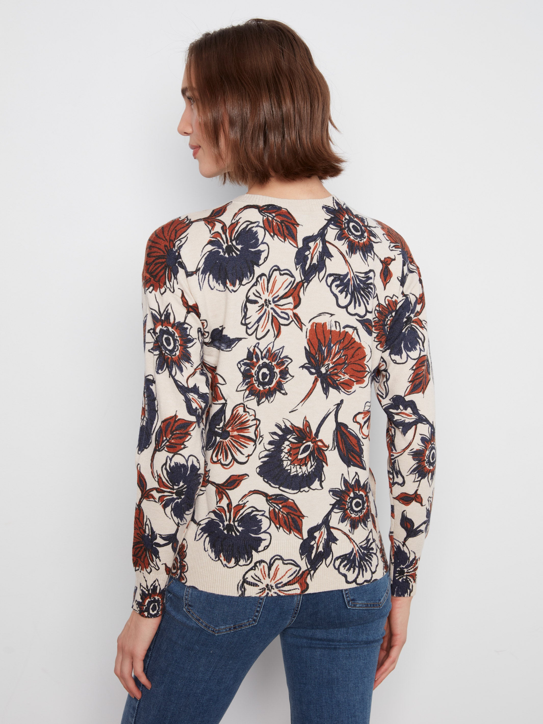 Back view of a long-sleeve sweater with large navy and rust floral prints on a cream background.