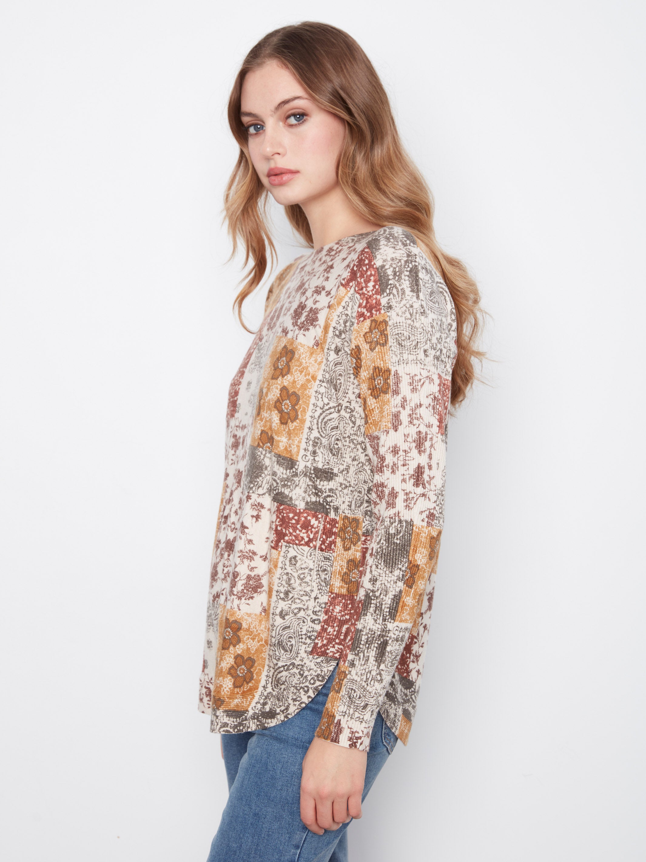 Long-sleeve patchwork patterned sweater in muted tones paired with blue denim jeans against a white background.