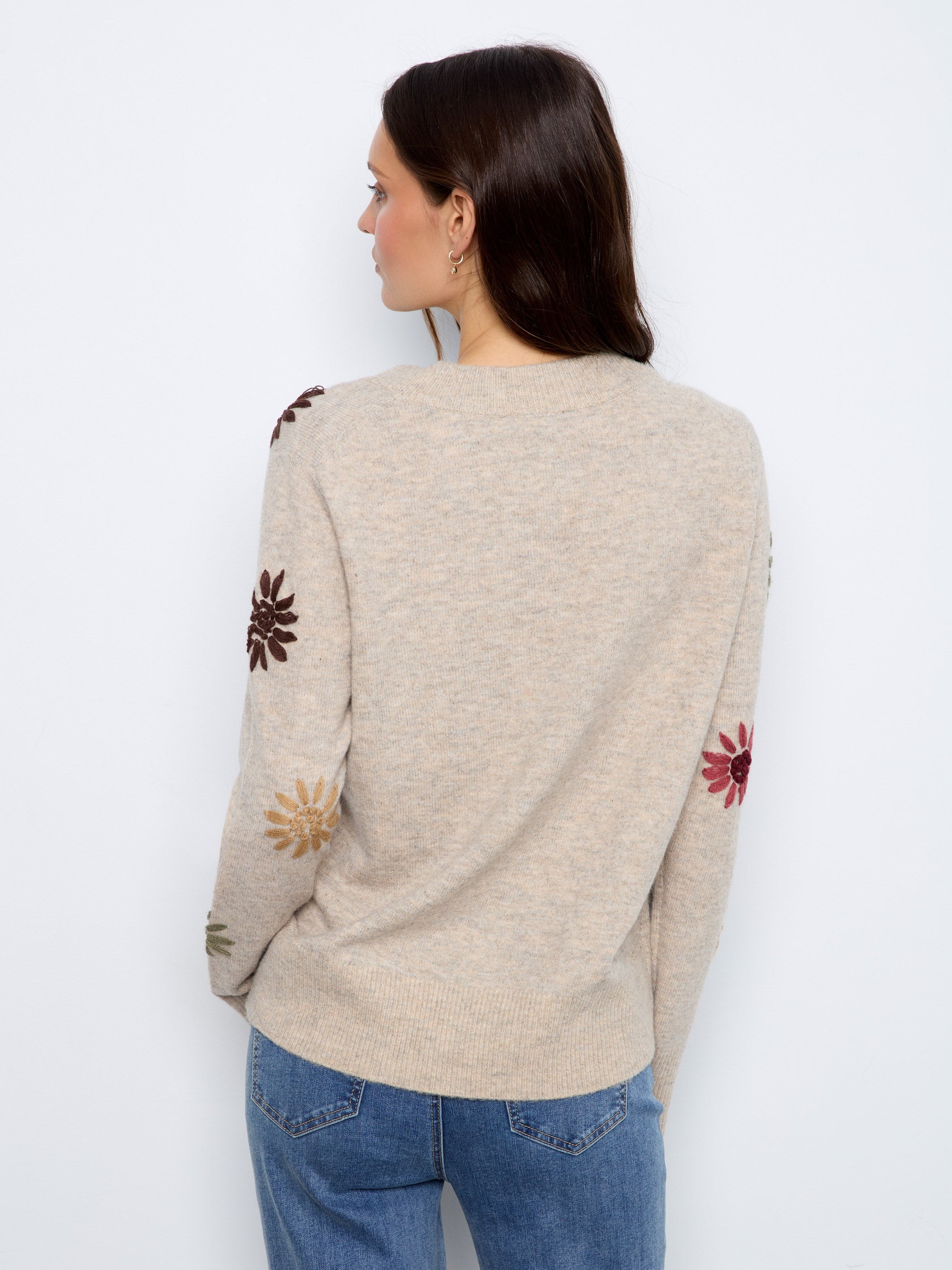 Light beige sweater with colorful floral embroidery on sleeves viewed from back against white background