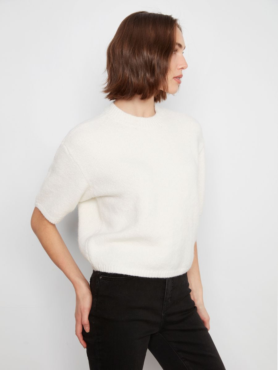 White short-sleeve knitted sweater paired with black high-waisted pants against a plain background.
