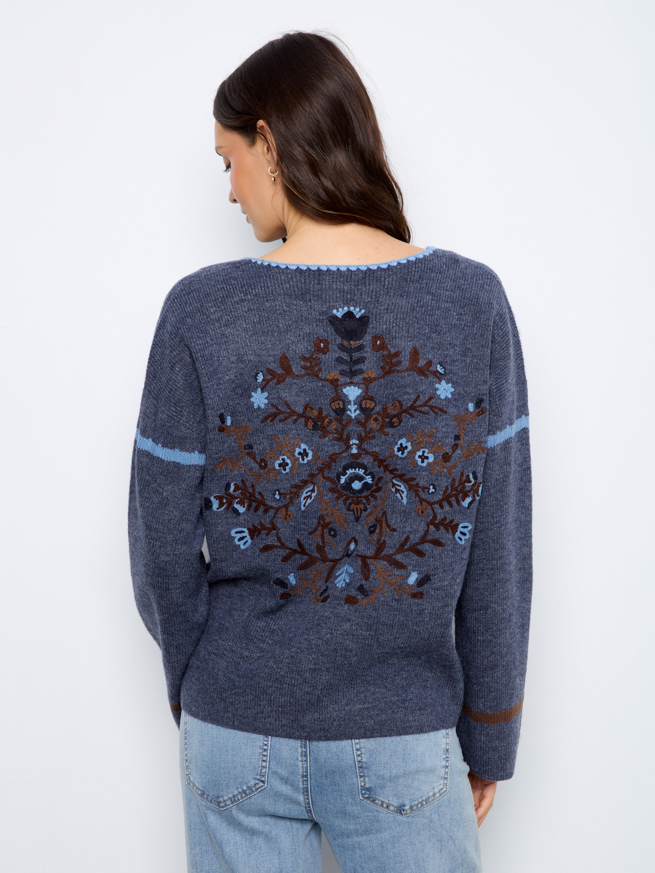 Back view of a blue knitted sweater with floral embroidery and light blue and brown stripes on sleeves.