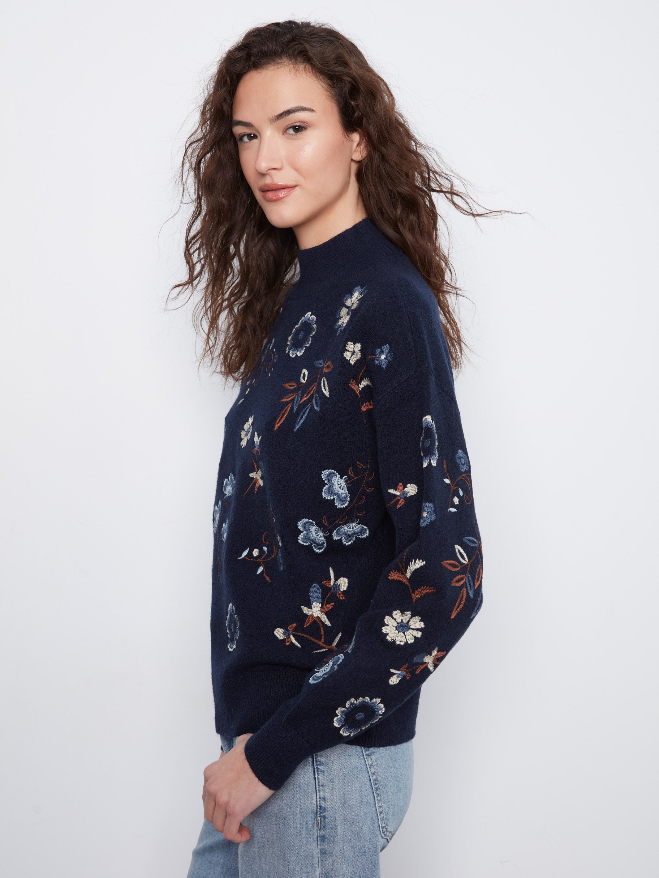 Navy blue sweater with floral embroidery paired with light blue denim jeans against a plain background